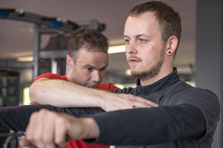 Schulungsleiter korrigiert Trainer bei der Ausführung einer Übung am Seilzug.