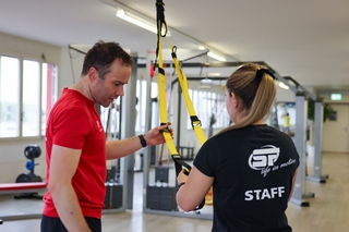 Der Kursleiter im roten T-Shirt zeigt dem STAFF Mitglied wie man das TRX einstellt.