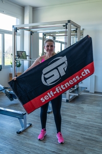 Eine Kundin präsentiert das self-fitness.ch Trainingshandtuch im Fitnessstudio.