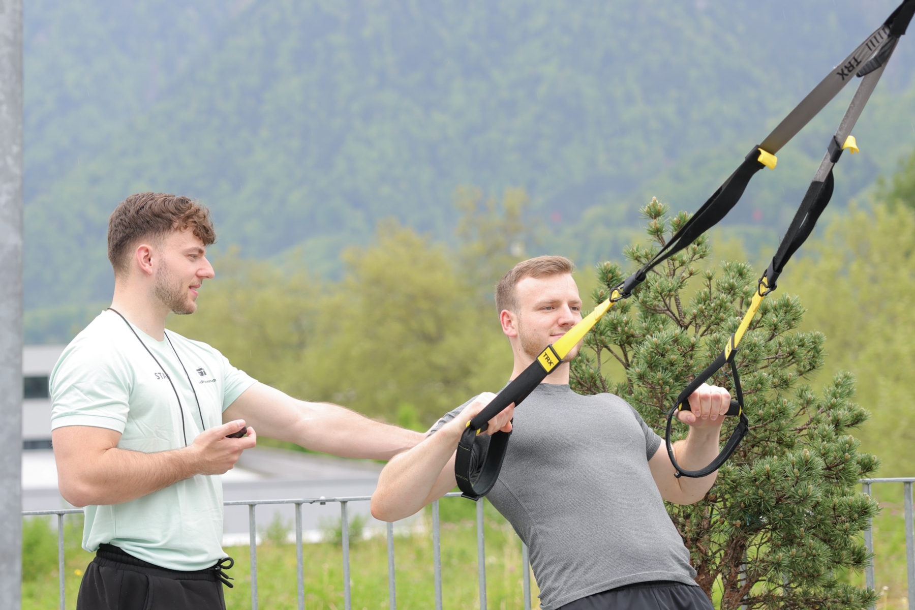 Trainer beim Instruieren eines Sportlers bei der Übung Rudern am TRX auf der Outdoor Terrasse in Interlaken.