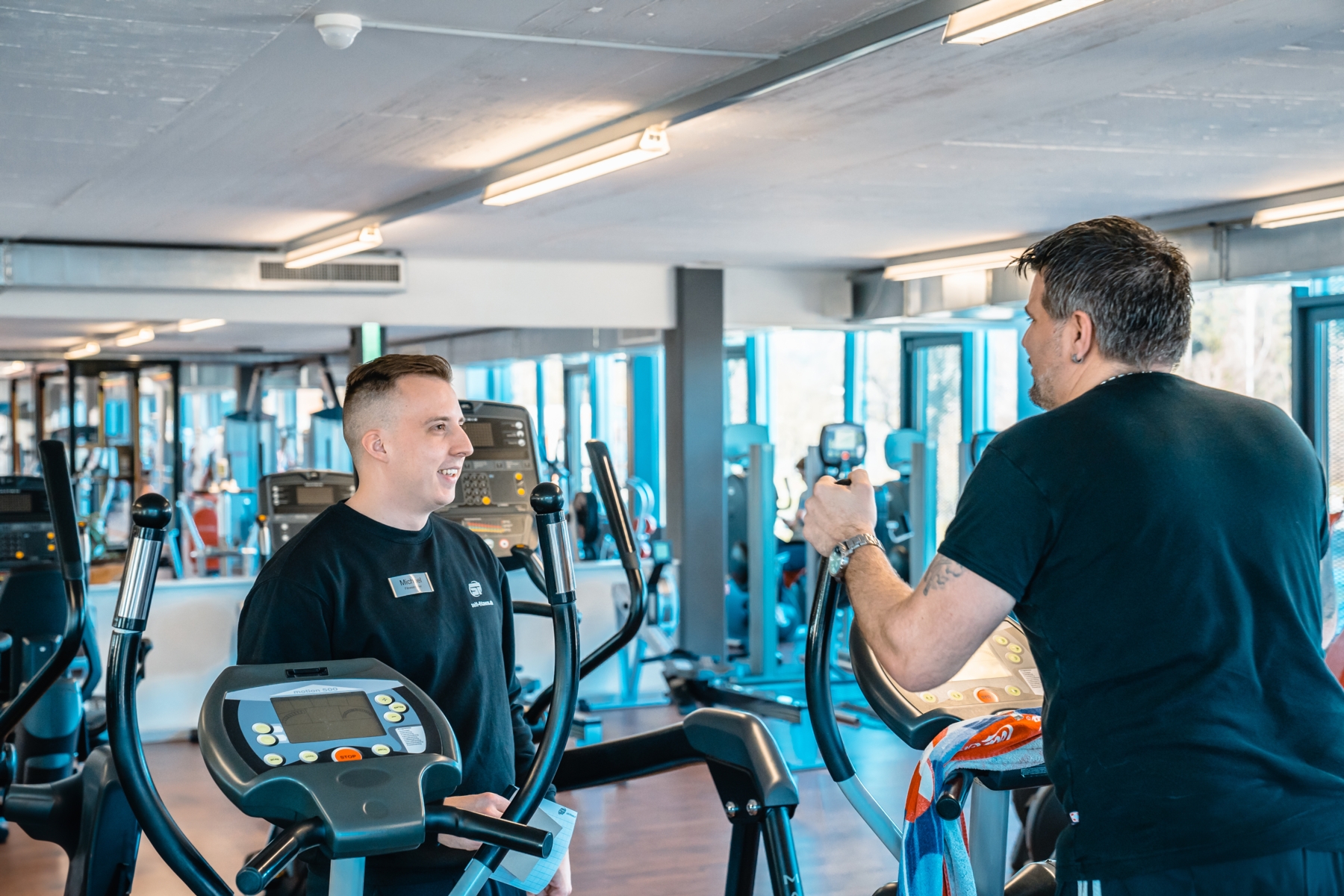 Trainer beim instruieren eines Sportlers auf dem Crosstrainer